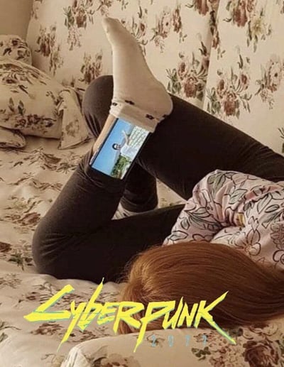 这是一张趣味搞笑的二次创作改图，主体内容为一名棕发人士仰躺在带有复古花卉图案的沙发上，身穿深色紧身长裤与带有卡通装饰的白色袜子，双脚抬起弯曲，用两只脚的脚掌夹住手机，正在观看手机屏幕播放的内容，姿势十分慵懒。图片下方叠加了经典游戏《赛博朋克2077》标志性的黄色锐利棱角风格logo，玩谐音梗调侃这种用脚操控电子设备的懒人行为如同使用了赛博义体，充满荒诞的科幻感，趣味性十足。