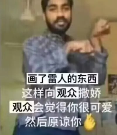 这是一张搞笑表情包，画面主体是一位留着络腮胡的南亚男子，他面带微笑，双手抬在胸前做出晃动手腕的撒娇动作，画面下方叠加了四行白色黑边的文字，内容为“画了雷人的东西 这样向观众撒娇 观众会觉得你很可爱 然后原谅你”，右下角还有一个黄色火焰emoji，整体内容是调侃创作者产出雷人内容后向观众撒娇求原谅的行为。