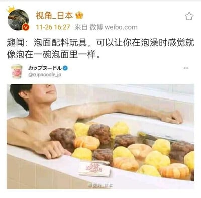 这是一张微博社交媒体截图，账号“视角_日本”于11月26日16:27发布了这条趣闻资讯，内容是介绍日本日清杯面推出的创意泡澡玩具。图中一名男性赤裸上身，放松地靠在浴缸边缘，双臂搭在浴缸外壁，神态惬意，浴缸内放置了大量模仿泡面常见配料（如肉块、虾仁、蛋块）造型的玩具，还有一个类似泡面调料包的物品，整体场景营造出仿佛泡在一碗巨大的日清杯面里的趣味效果，文案说明该玩具能让使用者在泡澡时拥有沉浸式的“泡在泡面里”的体验，充满创意和趣味性。