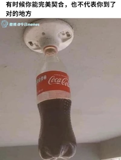 图片中展示了一个可口可乐塑料瓶被倒置，瓶口完美插入天花板上的一个白色固定装置（疑似灯具底座或挂钩）中，瓶身自然下垂，瓶内深色液体清晰可见。图片上方配有文字：“有时候你能完美契合，也不代表你到了对的地方”，通过日常场景中的视觉巧合，隐喻即使事物在形式上完美适配，也可能处于错误的位置或环境中，传达出一种关于适配与归属的生活哲理。