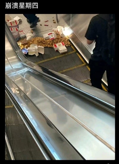 这张图展示了自动扶梯梯级上撒满了肯德基的食物，包括炸鸡块、包装盒、饮料杯等，旁边有行人路过，图片顶部配文“崩溃星期四”。这是对肯德基“疯狂星期四”营销梗的玩梗创作，将“疯狂”替换为“崩溃”，用食物撒一地的倒霉意外场景，呼应“崩溃”的情绪，既倒霉又充满笑点。
