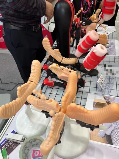 展会现场展示的多款假肢器械，包括不同类型的腿部假肢组件。展品具有仿真肤色的硅胶外层和复杂的机械关节结构，部分带有红色调节装置。背景中可见观众正在近距离观察这些医疗辅助设备，展示台上还摆放着相关的宣传资料和产品说明。
