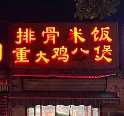 这是一张夜晚拍摄的街边饭店霓虹灯招牌照片，招牌上标注了两种餐品：排骨米饭和“重大鸡八煲”。其中“鸡八煲”是明显的书写失误，原本应该是“鸡煲”，错误的字样造成了不雅的歧义，让这个招牌显得十分滑稽搞笑，很容易吸引路人的注意，也成为了网友拍摄分享的趣味内容。