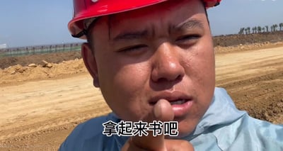 这是一张工地现场的实拍视频截图，画面中的小哥戴着红色安全帽，在烈日下满脸是汗，眉头紧皱、眼睛半睁，看起来工作得十分辛苦。他伸出一根手指对着镜头，配文“拿起来书吧”，以自己在工地从事体力劳动的亲身经历，真切地劝诫大家要好好学习，避免日后从事辛苦的体力工作，画面真实扎心，传递出对读书重要性的深刻感悟。