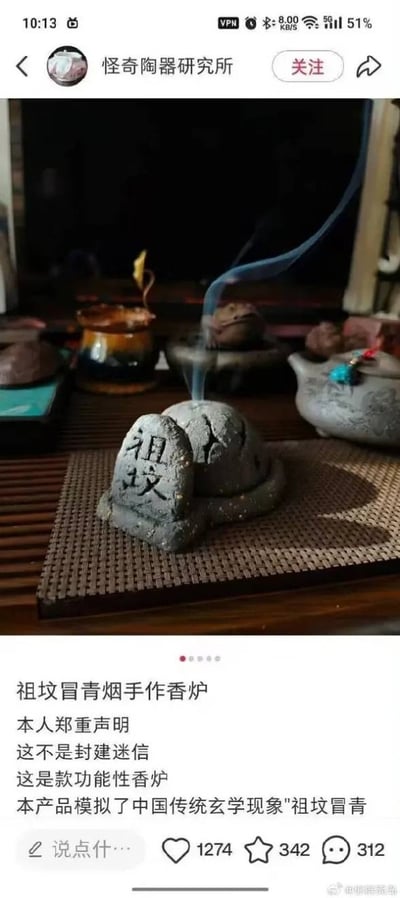 这是一张国内社交平台的帖子截图，发布账号为“怪奇陶器研究所”，内容展示了一款设计搞怪的手作香炉：香炉整体做成迷你祖坟的造型，旁侧立有刻着“祖坟”二字的小石碑，点香后烟雾从“坟堆”顶端冒出，恰好对应民间说法里的“祖坟冒青烟”。帖子配文玩梗式声明该产品不是封建迷信，是模拟传统玄学现象的功能性香炉，背景中还能看到茶席上摆放的其他茶壶、陶器摆件，截图底部显示该帖子获得1274次点赞、342次收藏、312条评论。