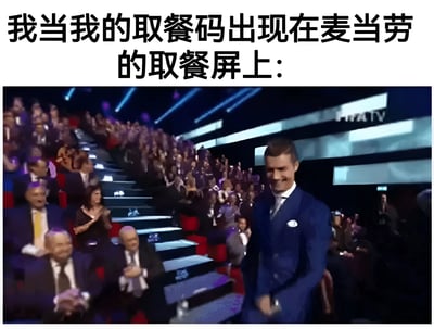 这张梗图上方配有文字“我当我的取餐码出现在麦当劳的取餐屏上:”，下方是一张颁奖典礼现场的照片。照片中一名穿着蓝色西装的男子正走上灯光璀璨的舞台，台下有大量观众起立鼓掌欢呼，背景屏幕上能看到“MTV”的标志。图片通过将看到自己取餐码出现的普通场景，夸张地类比为获得重大奖项的高光时刻，形成幽默效果。