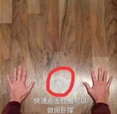 图片展示了一双真人的手撑在木地板上，双手之间有一个红色的圆圈。图片底部配有文字“快速点击红圈可以做俯卧撑”。这是一张带有幽默调侃性质的网络迷因图片，通过虚构“点击红圈即可做俯卧撑”的互动效果，制造出戏谑的笑点，实际上点击图片并不能真的完成俯卧撑动作。