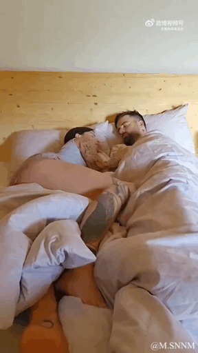 这是一个充满趣味的视觉错位动态图，画面初看是一对男女躺在床上相拥入眠，营造出亲密的情侣同床氛围。但随着画面的轻微变动，会发现实际上是三个人，中间的人被被子和姿势巧妙遮挡，制造出了两人同床的错觉，真相揭晓时让人忍俊不禁，十分滑稽。
