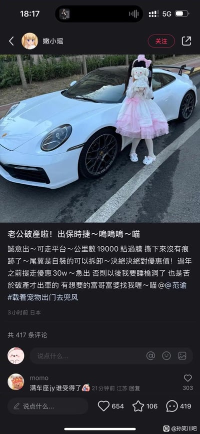 这是一张竖屏社交媒体截图，发布者「嫩小瑶」以卖萌的语气发布卖车动态，称老公破产，急出自己的白色保时捷，详细说明车辆情况：行驶19000公里、贴过膜无残留、自装尾翼可拆卸，过年前提车优惠30万，还调侃不出车就要睡桥洞，文案末尾带「喵」的卖萌语气词，并@了范詢，附带话题#载着宠物出门去兜风。配图是穿着粉白洛丽塔、抱着玩偶的女生靠在白色保时捷旁。
评论区热门评论「满车座jy谁受得了」玩了谐音梗，「座jy」谐音「做交易」，故意用低俗谐音制造戏谑笑点。