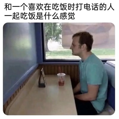 这是一张吐槽社交场景的梗图，上方配文点出核心主题，图中呈现了一位穿着蓝绿色短袖的男士独自坐在餐厅卡座餐桌旁的场景：长桌仅他所在的一侧有一杯带吸管的饮品，对面座位完全空着。用这种视觉化的方式，生动表达了当与吃饭时只顾打电话、无视同伴的人一起用餐时，自己仿佛被彻底忽略、如同独自吃饭的尴尬、落寞与无奈，精准戳中了这类社交场景里的不适体验，引发有类似经历者的共鸣。