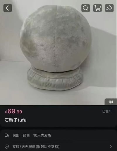 这是一张电商平台的商品展示截图，展示了一款名为"石墩子fufu"的灰色毛绒玩具。玩具呈球形，表面有类似石墩纹理的设计，底部有一圈褶皱边缘。商品售价为69.99元，已售出15件，支持包邮和预售，10天内发货，并支持7天无理由退货(拆封后不支持)。界面上方有常见的电商功能按钮：返回、搜索、购物车和分享。