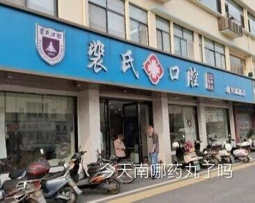 这是一张裴氏口腔线下门店的实拍照片，蓝色的门店招牌上印有白色的“裴氏口腔”字样及品牌标识，门口停放着多辆电动车，还有两位路人站在店门口。图片底部被添加了文字“今天南哪药丸了吗”，其中“南哪”是“南京大学”的谐音，“药丸”是“要完”的谐音，再结合门店名称“裴氏”谐音“赔氏”，形成多层谐音梗，用来调侃相关内容。