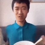 动图中一名穿着蓝色衬衫的男子正端着白色饭碗，手持筷子，身体微微晃动，脸上的笑容逐渐加深，看起来正津津有味地享用食物，整体氛围轻松愉快，充满生活气息。