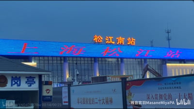 傍晚时分的上海松江南站户外场景，建筑顶部亮着“松江南站”的红色发光标识，下方电子屏显示“上海松江站”字样；前景有蓝白配色的岗亭，以及带有“学习贯彻党的二十大精神”“松江，我们的美丽家园 正在创建全国文明城区”等宣传内容的施工围挡，围挡上还有“安全用电”警示标识，建筑旁可见施工设备与通信基站，整体呈现出车站的日常户外状态。