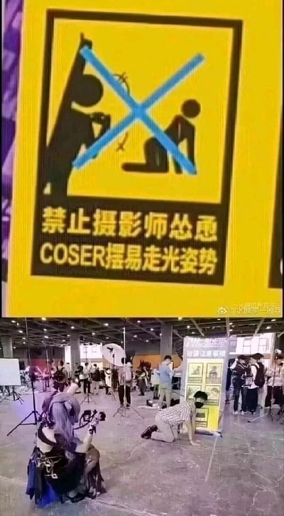 这张图片由上下两部分构成，上方是漫展现场设置的黄色警示标识，标识内有被蓝色叉号明令禁止的图示：一名摄影师正对一名摆出易走光姿势的COSER，下方配有明确的文字提示“禁止摄影师怂恿COSER摆易走光姿势”，旨在规范漫展摄影行为，保护COSER的个人权益。下方是漫展的真实拍摄场景，一名身着《原神》角色COS服装的女性COSER手持相机，对着一名跪在地上、身体前倾摆出类似标识中被禁止姿势的男性摄影师，现场还分布着其他摄影设备和参与漫展的人群，背景中可见漫展的相关提示展板。整个现场场景是对上方警示标识的反向复刻，形成了强烈的反差感，属于漫展参与者的玩梗行为，制造出趣味十足的效果。
