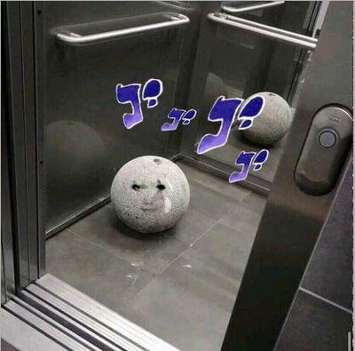 这是一张经过P图改编的趣味梗图，场景设定在狭小的电梯内部，一个原本普通的石球被P上了委屈又局促的人脸表情，电梯镜子的反射效果让石球看起来仿佛被困在封闭空间里。图中还添加了紫色的日语拟声词“ゴ”（常用于表现沉重、压抑或紧张的氛围），将石球完全拟人化，生动地还原了社恐人群身处封闭狭小空间时的窘迫与不安，充满搞笑感。