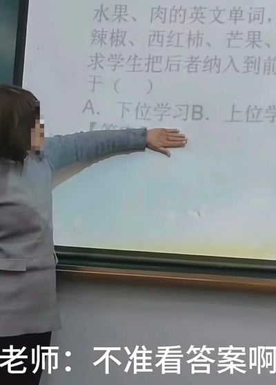 这是一张课堂实拍的静态图，画面中一位女老师背对着镜头，面部被打码，她伸出手臂，手掌摊开挡住投影屏幕上的部分内容。投影屏幕上显示一道教育心理学相关的选择题，内容为“水果、肉的英文单词，辣椒、西红柿、芒果、求学生把后者纳入到前于（ ）A. 下位学习B. 上位学”，题目内容有部分截断。图片底部配有白色字幕“老师：不准看答案啊”，老师的手看似是要挡住题目答案，但位置刚好在选项区域，形成了有趣的反差感，展现了课堂上的搞笑日常。