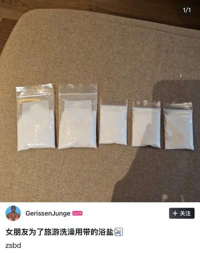 这张图是社交媒体发帖截图，上半部分为实拍内容，五个大小不一的透明自封袋内装着白色粉末状的浴盐，整齐摆放在浅棕色的布艺沙发表面，这类包装常让人联想到违禁物品；下半部分是用户GerissenJunge的发帖内容，配文称这些粉末是女朋友为旅游准备的洗澡用浴盐，结合原标题“放行李里头不好解释，绑身上吧”的调侃，制造出反差笑点，暗指这类包装的白色粉末如果放在行李中过安检，极易被误认为是违禁品，难以解释清楚。
