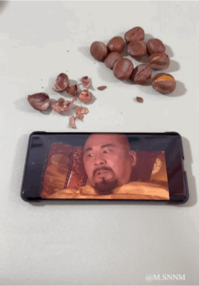 这是一个充满创意的动态错位梗图，将现实中剥栗子的动作与经典宫斗剧《甄嬛传》的名场面巧妙结合：拿起带壳栗子对应手机里躺着的皇上，仿佛“剥去龙袍”；剥开栗子壳露出栗仁时，手机画面切换为甄嬛，恰似“露出真身”；最后将栗仁放置一旁，手机画面切到皇上驾崩的场景，趣味还原甄嬛毒杀皇上的名场面，通过视觉错位制造出剧情联动的搞笑反差感。