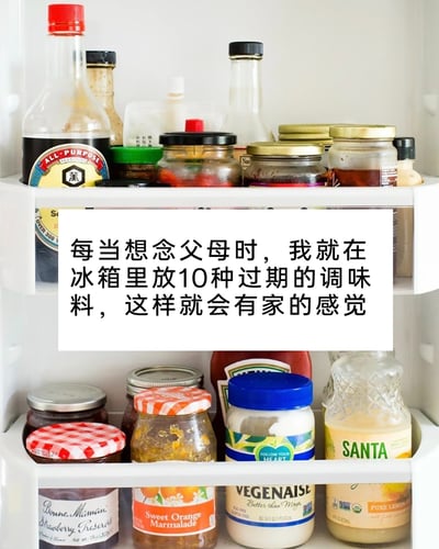 这是一张图文混排的静态图片，背景为冰箱门的白色隔层，隔层里摆放着多种玻璃瓶装的调味料，包括酱汁、果酱、调味酱等，瓶身样式和标签各不相同，呈现出家庭冰箱的日常状态。图片中间有一个白色的文字框，框内写着一段充满亲情温度的文字：“每当想念父母时，我就在冰箱里放10种过期的调味料，这样就会有家的感觉”，通过捕捉家庭中常见的“留存过期调味料”这一细节，将对父母和家的思念具象化，用贴近生活的方式引发游子的情感共鸣。