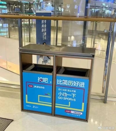 这是一张拍摄于商场内的实拍图，画面主体是一个双投放口的金属垃圾桶，桶身外侧贴有小红书「大家运动会」的活动宣传标语。左侧投放口标语为「投吧，大家运动会」，右侧投放口标语为「比简历好进 扔个垃圾 怎么不算 小动一下 GO SPORIS」。该内容玩了职场相关的梗，将扔垃圾的「投」与投简历的「投」关联，用「比简历好进」吐槽当下职场求职的艰难，把日常扔垃圾的行为包装成「小动一下」的运动环节，贴合「大家运动会」的活动主题，用轻松搞笑的方式赋予普通垃圾桶趣味性，引发职场人的共鸣。