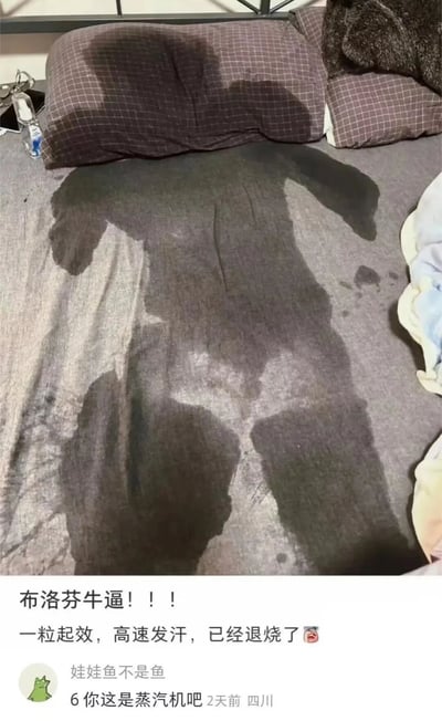 图片展示了一张床，床垫上有一个清晰的人形深色汗渍，面积较大，形状酷似人体平躺时的轮廓，显示出使用者在睡眠中大量出汗的状态。图片下方配有文字内容，主文为“布洛芬牛逼！！！一粒起效，高速发汗，已经退烧了”，表达了对布洛芬退烧效果的认可，强调其快速发汗退烧的作用。下方还有一条来自用户“娃娃鱼不是鱼”的评论：“你这是蒸汽机吧”，以幽默夸张的方式调侃出汗量之大，如同蒸汽机一般。整体内容通过真实的汗渍图片与文字结合，生动展现了服用布洛芬后大量出汗退烧的经历，带有轻松诙谐的氛围。
