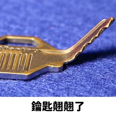 这是一张玩谐音梗的趣味图片，画面主体是一把齿部向上翘起的金属钥匙，放置在蓝色绒面材质的背景上。图片下方配有繁体文字“鑰匙翹翹了”，利用“钥匙翘翘”与“要死翘翘”的谐音关系，调侃事情搞砸、处境糟糕的状态，用实物钥匙的形态巧妙呼应文字的谐音含义，充满戏谑感。
谐音梗说明：“钥匙翘翘”谐音“要死翘翘”，是中文网络里用来表达事情完蛋、情况不妙的调侃说法。