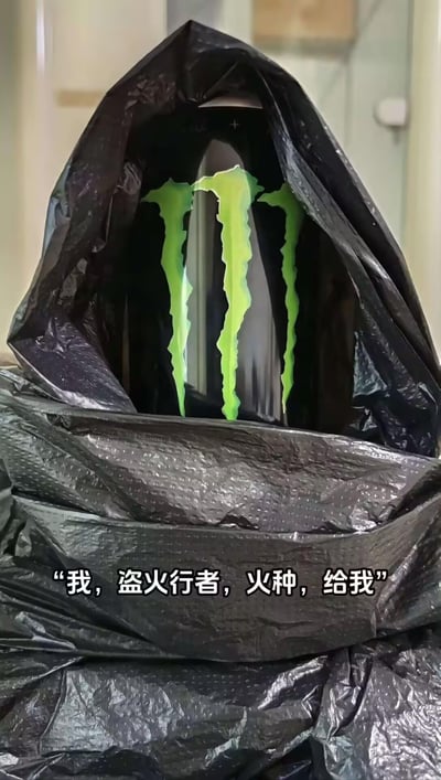 这是一张创意整活梗图，用黑色塑料袋将魔爪（Monster Energy）能量饮料包裹成带兜帽的神秘造型，搭配《艾尔登法环》中“盗火行者”的台词“我，盗火行者，火种，给我”，把魔爪饮料的标志性绿色爪印标志和“能量火种”的概念结合，玩了造型模仿和台词梗，营造出搞笑又神秘的反差感。