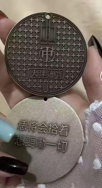 图片展示了两枚圆形金属文创纪念牌，上方的纪念牌模仿古钱币形制，表面布满十字格纹理，刻有“大豫通宝”字样、“申”字，还有一座类似河南地标建筑的图案；下方的纪念牌刻有河南方言文字“恁将会拾着想要嘞一切”，传递出“你将会得到想要的一切”的美好祝福。
方言说明：“恁”是河南方言中“你”的称呼，“嘞”对应普通话的“的”，“拾着”在方言语境里表示“获得、得到”，充满地域文化特色。