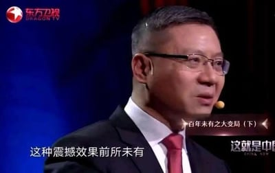 这是东方卫视政论节目《这就是中国》的视频截图，画面中的人物是学者张维为，他身着深色西装、佩戴眼镜，正处于演讲的状态，神情专注。画面上分布着多处文字信息：左上角是东方卫视的台标及英文名称“DRAGON TV”，画面右侧标注了当期节目环节“百年未有之大变局（下）”，右下角是节目名称“这就是中国 CHINA NOW”，底部配有演讲字幕“这种震撼效果前所未有”，整体呈现出专业严肃的政论节目观点输出场景。