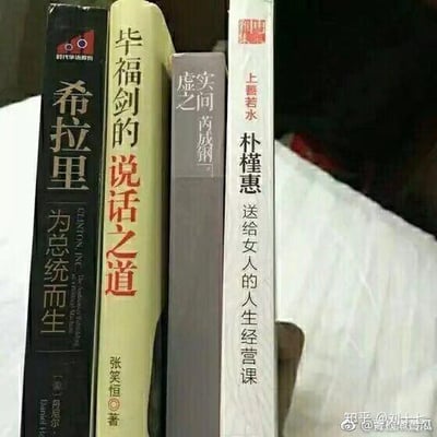 这是一张通过摆放四本不同人物相关书籍，利用书脊文字的错位组合制造笑点的趣味梗图。四本书的书脊文字分别为《希拉里 为总统而生》《毕福剑的说话之道》《虚实之间 芮成钢》《上善若水 朴槿惠 送给女人的人生经营课》，将书脊上的人物名字部分连读，形成带有调侃意味的组合，属于典型的书脊文字拼接类趣味创作。