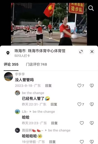 图片展示了珠海市体育中心体育馆外，一群身着红色上衣、黑色短裤的徒步队成员在夜间列队行进的场景。队伍整齐有序，前方有人高举写有“美丽珠海徒步队”的红色旗帜。图片下方是社交媒体平台的评论区，显示该地点有5013人打卡，355条评论。有网友评论“没人管管吗”，随后有人回复“已经有人管了”并配了一个哭笑不得的表情，引发其他网友一连串的“哈哈”回应。