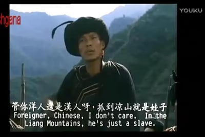 图片为一段影视视频截图，画面中一名身着传统服饰、头戴黑色帽子的男子站在连绵的山脉背景前。人物表情严肃，下方配有中英文字幕，中文内容为“管你洋人还是汉人呀，抓到凉山就是娃子”，英文翻译为“Foreigner, Chinese, I don't care. In the Liang Mountains, he's just a slave.”。整体场景展现了具有地域特色的历史或民俗情境。