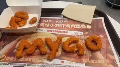 这是一张创意美食摆拍图，展示了肯德基与长沙文和友联名的餐品场景：托盘上放着印有「KFC | 长沙文和友 虾风味小龙虾烤鸡腿堡 连续7年陪你跨年」字样的餐垫纸，餐垫纸上用肯德基炸制小食摆成了「MYGO」的英文单词；左侧打开的肯德基小食盒里还剩余几块同款炸物，旁边配有纸巾。整体是用户将餐食进行趣味摆放的创作，充满创意感。