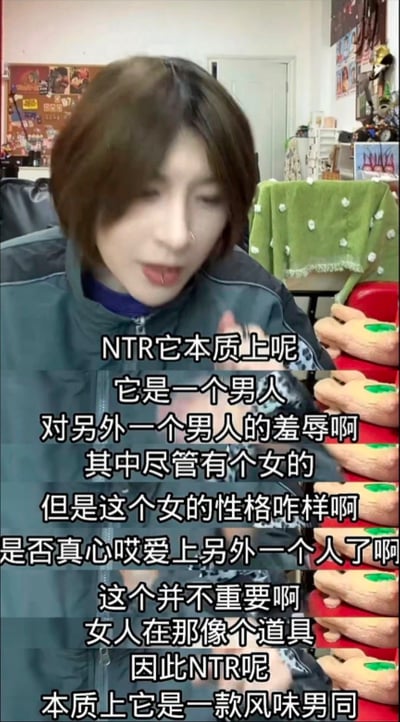这是一张视频截图，显示一位短发人士正在讨论NTR的本质。画面中人物穿着深色外套，背景是一个布置有绿色毯子和毛绒玩具的房间。图中叠加了大量文字，主要观点认为NTR本质上是一个男人对另一个男人的羞辱，女性角色在其中更像道具而非关键因素，并将其形容为"风味男同"。