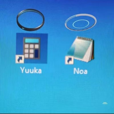 这是一张围绕游戏《蔚蓝档案》角色制作的桌面玩梗图，背景为蓝色电脑桌面，左侧是标注为“Yuuka”的计算器样式快捷方式图标，上方搭配黑色镜头滤镜环，对应游戏中以相机为标志性道具的角色早濑优香；右侧是标注为“Noa”的书本样式快捷方式图标，上方搭配白色天使光环，对应游戏中的天使角色诺亚。图中通过将角色的核心特征与桌面图标结合，玩出角色相关的趣味梗，右下角带有PhotoGrid的编辑水印。