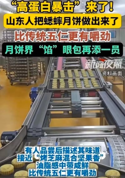 图片展示了工厂内的月饼生产线场景，传送带上整齐排列着待加工的月饼。画面上方有醒目的黄色和红色文字标题“高蛋白暴击来了！山东人把蟋蟀月饼做出来了”，强调这是一款创新月饼。中间文字“比传统五仁更有嚼劲 月饼界‘馅’眼包再添一员”中，“馅眼包”是谐音梗，将“显眼包”（指引人注目、爱出风头的人或事物）中的“显”替换为“馅”（月饼馅料），调侃这款蟋蟀月饼是月饼界中引人注目的新馅料成员。底部文字则描述了品尝感受：“有人品尝后描述其味道接近‘烤芝麻混合坚果香’ 油脂感中带咸鲜 比传统五仁更有嚼劲”，进一步介绍产品特点。