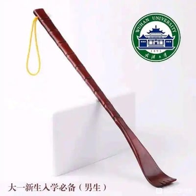 这是一张图文混排的单图，画面主体是一款仿竹节造型的深棕色木质痒痒挠，顶端带有黄色挂绳；右上角放置着武汉大学的圆形校徽，校徽内包含学校英文名称、建校年份1893以及标志性建筑图案和中文校名；图片底部配有文字“大一新生入学必备（男生）”。这张图是一个谐音玩梗图，利用“武汉大学”的“武大”谐音“武大郎”，而痒痒挠常被关联到武大郎的经典形象，以此制造趣味调侃效果，针对武汉大学的男新生进行玩笑式的调侃。
