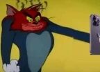 图片中是经典动画《猫和老鼠》里的角色汤姆，它呈现出愤怒的表情，双眼圆睁，耳朵向后竖起，一只手正举着手机，背景为黄色。整体画面捕捉了汤姆情绪激动的瞬间，是动画中的经典场景截图。