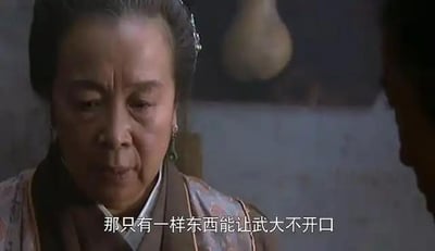 这是1998版电视剧《水浒传》的截图，画面中饰演王婆的演员神色凝重，正与对面的人密谋，屏幕下方的字幕显示“那只有一样东西能让武大不开口”，这段内容出自剧中王婆、西门庆、潘金莲合谋，计划让发现二人私情的武大郎永远闭嘴的情节，充满了狡诈的阴谋感。