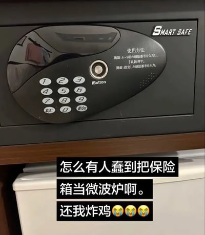 这张图的上半部分是黑色智能保险箱的控制面板特写，面板上带有数字按键、iButton感应区，右上角标注有SMART SAFE字样，面板上还印有日文的保险箱使用说明。图的下半部分叠加了黑底白字的吐槽文案，内容为“怎么有人蠢到把保险箱当微波炉啊。还我炸鸡”，后面搭配了三个流泪大哭的表情，整体是分享生活中发生的乌龙搞笑事件，吐槽他人误把保险箱当成微波炉放置炸鸡，导致炸鸡被锁无法取出的尴尬搞笑状况。