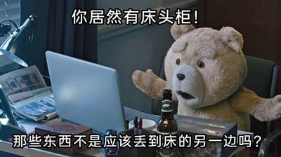 这张图是对美国喜剧电影《泰迪熊》的截图进行改编后的梗图，图中的毛绒泰迪熊坐在摆放着笔记本电脑、报纸、酒瓶的桌前，摊开双手，脸上露出惊讶又不可置信的表情。图中添加了两行中文台词：“你居然有床头柜！那些东西不是应该丢到床的另一边吗？”，以幽默夸张的方式调侃部分人没有使用床头柜收纳物品的习惯，而是把随手物品直接扔到床的另一侧，用泰迪熊的夸张反应放大了这种生活细节的搞笑感，引发有相同习惯的人的共鸣。