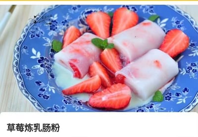 这是一张美食图片，展示了在蓝色花纹瓷盘上的草莓炼乳肠粉。盘中肠粉呈卷状，里面夹着新鲜草莓块，旁边摆放着切好的草莓和薄荷叶点缀，表面淋有炼乳，整体看起来像甜品风格。画面视觉冲击力很强，肠粉通常是粤式咸点，这里与草莓和炼乳混搭，带有明显的中西结合搞怪感。

暗示/谐音梗：肠粉本来是咸食，这里做成甜品，有一种“甜咸混搭”的反差趣味，容易成为朋友圈吐槽或美食黑暗料理梗图。