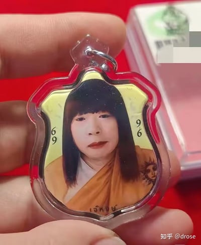 这是一款模仿泰国佛牌样式制作的趣味吊坠，创作者将泰国知名高僧龙婆坤的形象通过P图改成了齐刘海长发的女装造型，封装在带有红色边缘的异形透明外壳中。图像左右标注了数字“69”“96”，底部还有泰文标识，整体是对传统宗教佛牌的搞笑恶搞，充满戏谑趣味。