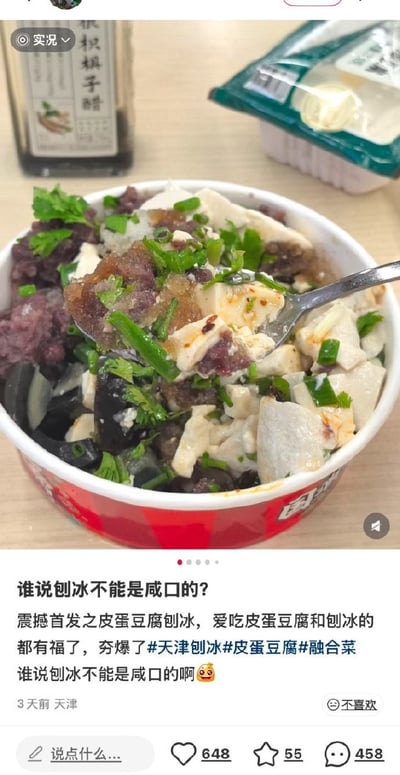 这是一则社交媒体动态截图，画面上半部分展示了一碗创意食物，碗中混合了甜口刨冰常见的碎冰、红豆，同时搭配了中式凉菜皮蛋豆腐的食材：嫩豆腐块、皮蛋碎，还撒了葱花、香菜调味，旁边桌面摆放着一瓶根积棋子醋和一盒未开封的食物。动态配文调侃这款食物是天津首创的咸口皮蛋豆腐刨冰，称爱吃皮蛋豆腐和爱吃刨冰的人都会喜欢，属于融合类创意菜品，打破了大众认为刨冰都是甜口的固有印象，该动态收获了648赞、55次收藏和458条评论。