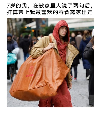 这是一张搞笑的图文梗图，上方配文描述了7岁的自己被家人批评两句后，赌气要带着最喜欢的零食离家出走的童年场景；下方的图片是一位穿着红色连帽衫外搭卡其色外套的成年人，单肩扛着一个尺寸夸张的棕色皮质包，表情委屈又故作坚定，行走在人流密集的街道上。用成年人的夸张造型来还原小孩赌气时，把少量零食当作“全部家当”的幼稚心态，通过场景和人物状态的反差，制造出幽默搞笑的效果，引发网友对童年类似经历的共鸣。