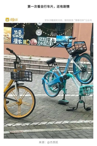 这是一张街头实拍的趣味图片，几辆共享单车因停放位置巧合形成视觉错位：右侧的哈啰单车看起来像是“骑”在另一辆车上，旁边的美团单车则像在“围观”，搭配背景店铺的“摆烂艺术家”“禁止蕉绿（谐音焦虑）”等潮流标语，营造出仿佛有剧情的搞笑场景，被网友调侃是“第一次看有剧情的自行车片”。
没有双关或谐音梗，核心是视觉错位带来的脑洞趣味。
