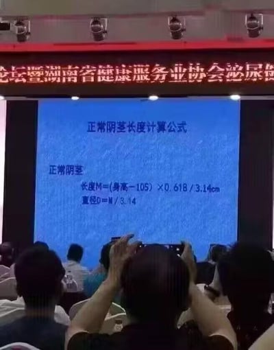 图片显示的是一个会议现场，背景有红色横幅写着“论坛暨湖南省健康服务业协会泌尿”。前方大屏幕上展示着“正常阴茎长度计算公式”，具体公式为：长度M=(身高-105)×0.618/3.14cm，直径D=N/3.14。台下有多位观众，部分人正在用手机拍摄屏幕内容。