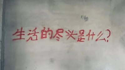 这是一张原始拍摄的竖版图片，画面主体是一面带有污渍的浅色墙面，墙面上用红色颜料手写着一行略显潦草的问句“生活的尽头是什么？”，字体带着一种随性又迷茫的质感。这句提问传递出书写者对生活感到困惑、迷茫的情绪，像是在经历生活的压力与疲惫后发出的灵魂拷问。对于这个问题，其实没有统一的标准答案：它可以是我们在日常烟火里找到的专属意义，是每一次微小的快乐、每一份踏实的满足堆积起来的温暖日常；也可以是我们最终与生活和解，接纳所有的遗憾与圆满，过上让自己内心安定的日子；它更可能是没有“尽头”，而是一场不断前行、不断与自己对话的漫长旅程。