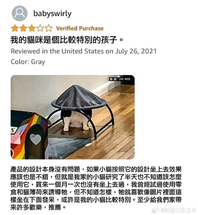 这是一张社交媒体截图，内容为用户“babyswirly”的产品评价。用户表示自己的猫咪比较特别，购买的灰色猫窝设计本身没问题，但猫咪研究半天也不会正确使用，一个月来从未坐上去过，反而喜欢坐在猫窝下面发呆。配图中可以看到一只猫正坐在灰色猫窝下方的地板上，旁边还有一个彩色的物品。用户称猫咪的这种行为给家里带来了许多欢乐，并推荐该产品。
